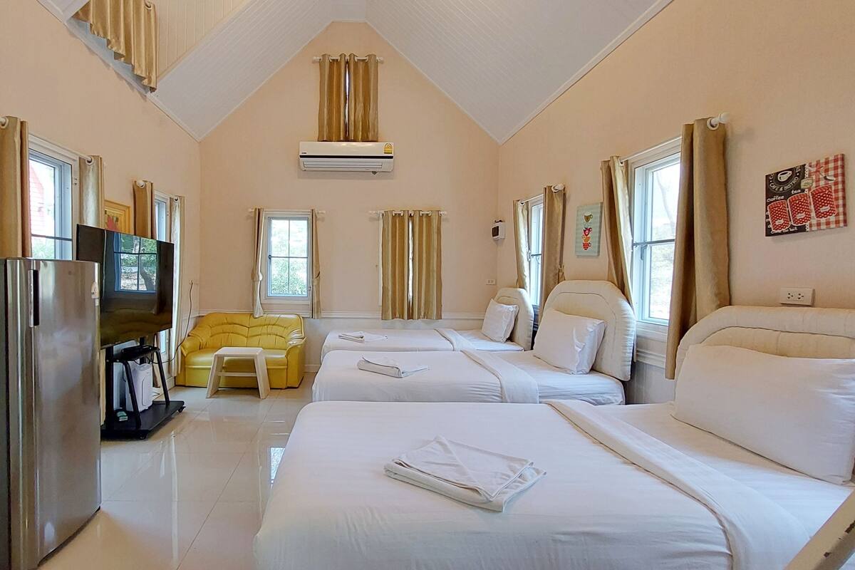 A hotel room with two beds, a yellow armchair, a television, and an air conditioning unit.