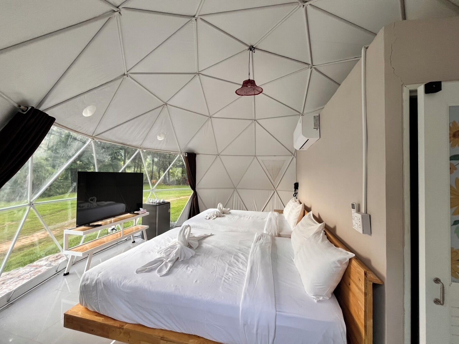 A modern tent-style room with a bed, a TV, and a view of the outdoors.