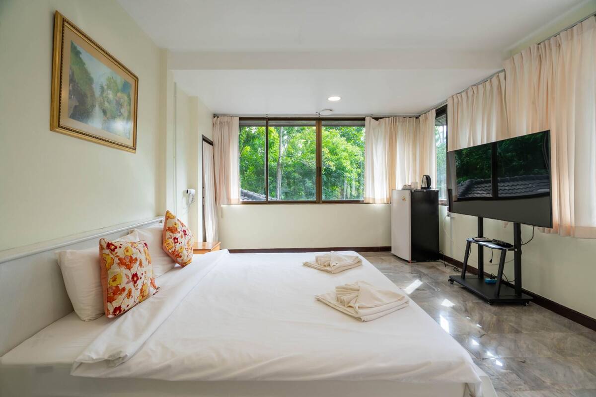 A hotel room with a bed, a TV, and a window with curtains.