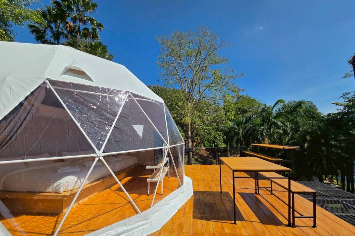 A geodesic dome tent on a wooden deck with a table and chairs, surrounded by trees.