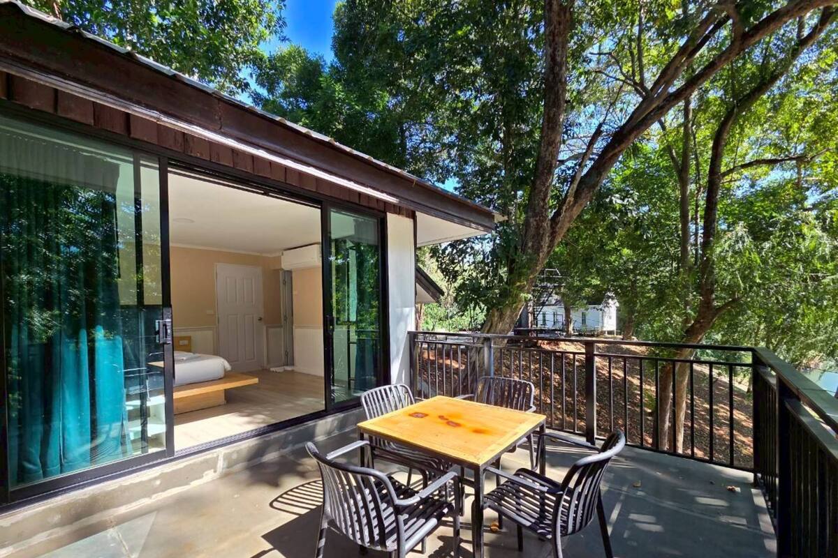 A modern outdoor patio with a wooden table and metal chairs, overlooking a lush garden and a residential area.