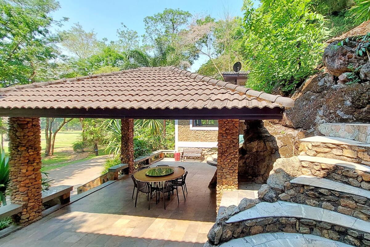 A covered outdoor seating area with stone pillars, a stone wall, and a view of the surrounding greenery.