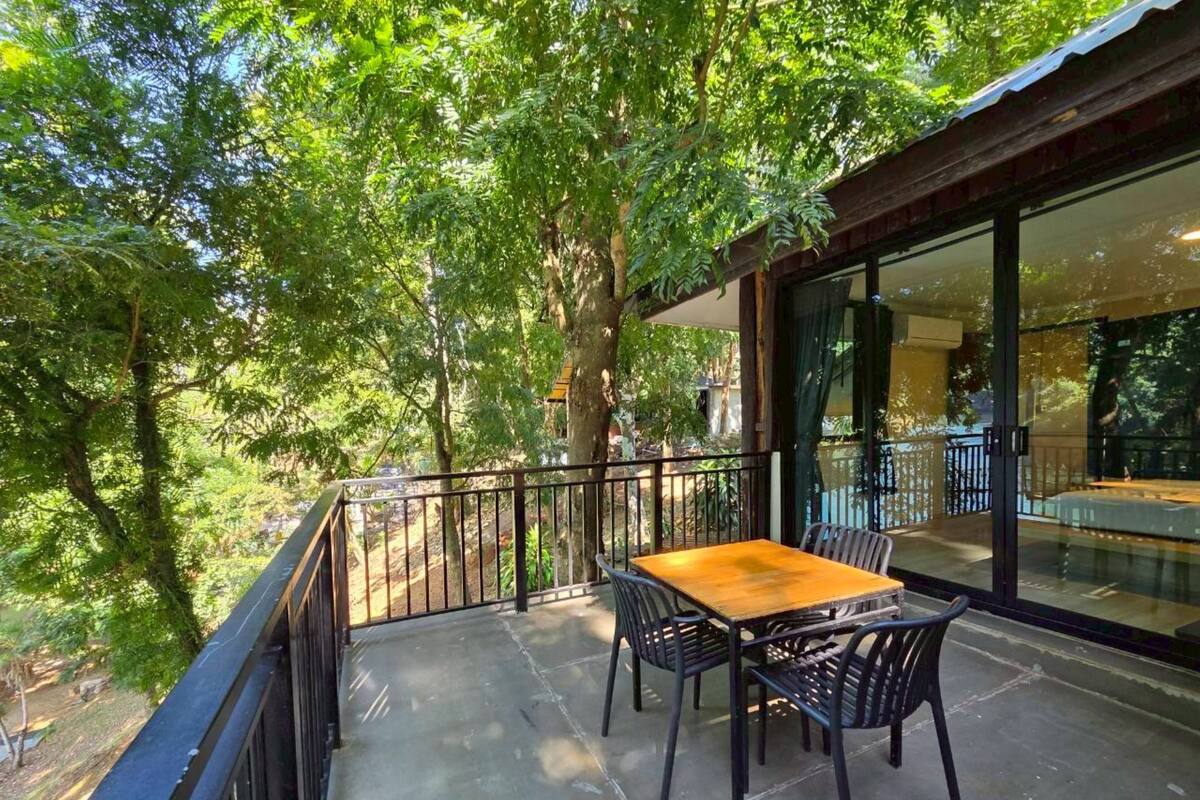 A balcony with a table and chairs, surrounded by trees and a glass wall.