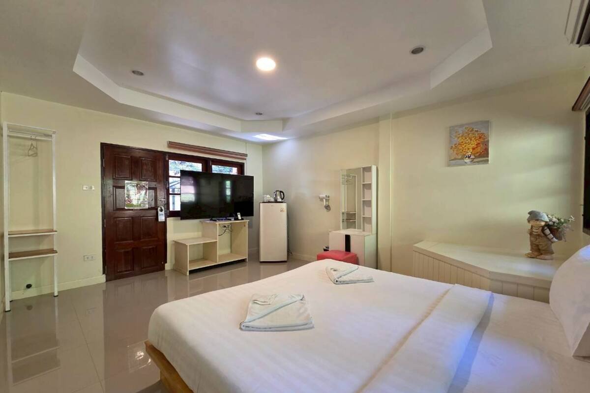A hotel room with a large bed, a television, a refrigerator, a vanity with a mirror, and a small decorative figure.