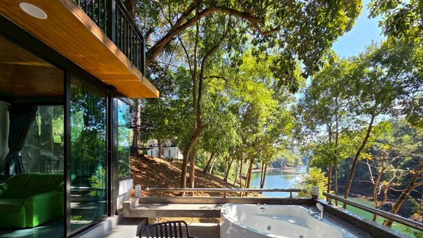 Ein moderner Außenbereich mit Whirlpool, einer Glasreling mit Seeblick, umgeben von Bäumen und einer Holzterrasse.