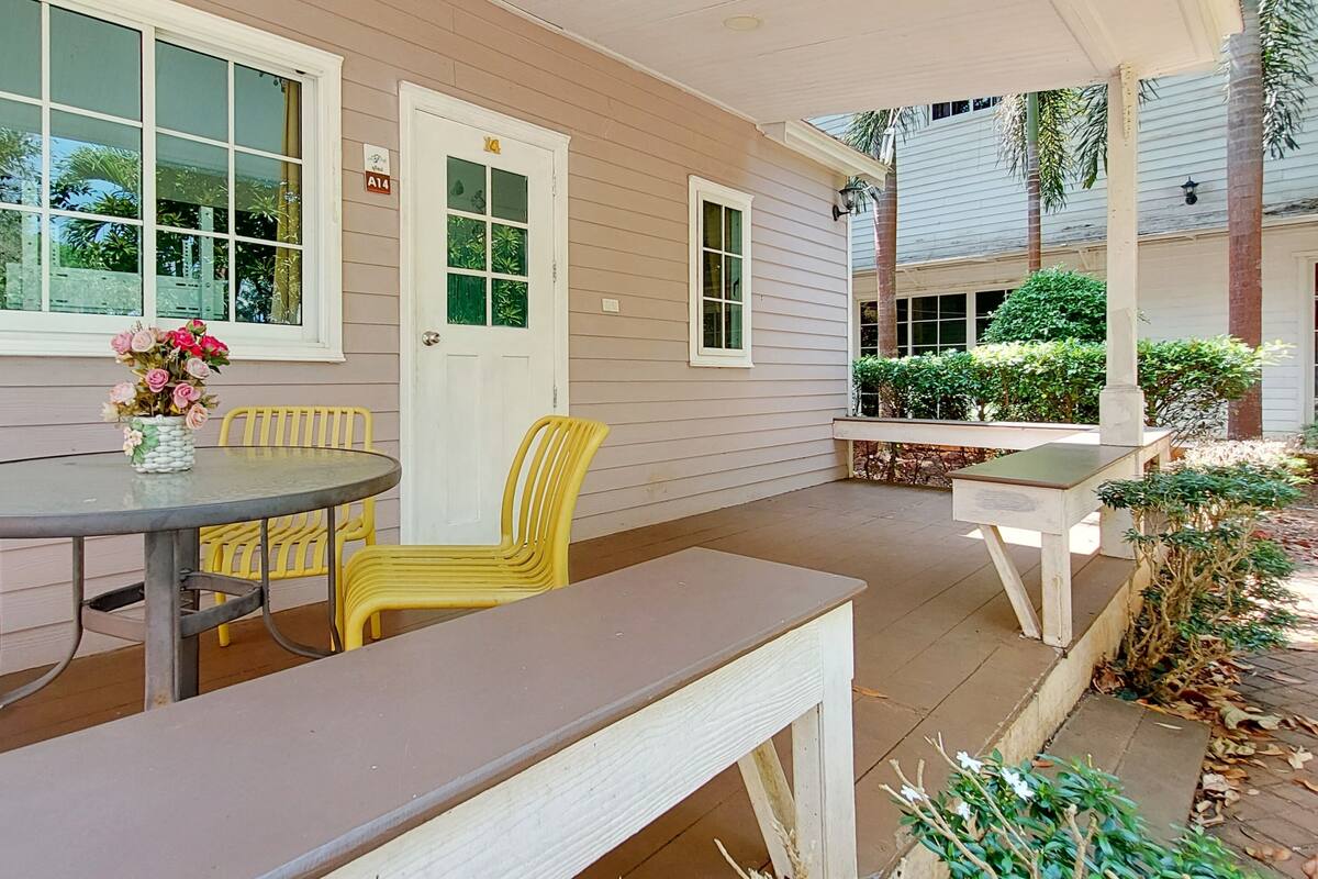 A patio with a round table, yellow chairs, a bench, and a door with a window.