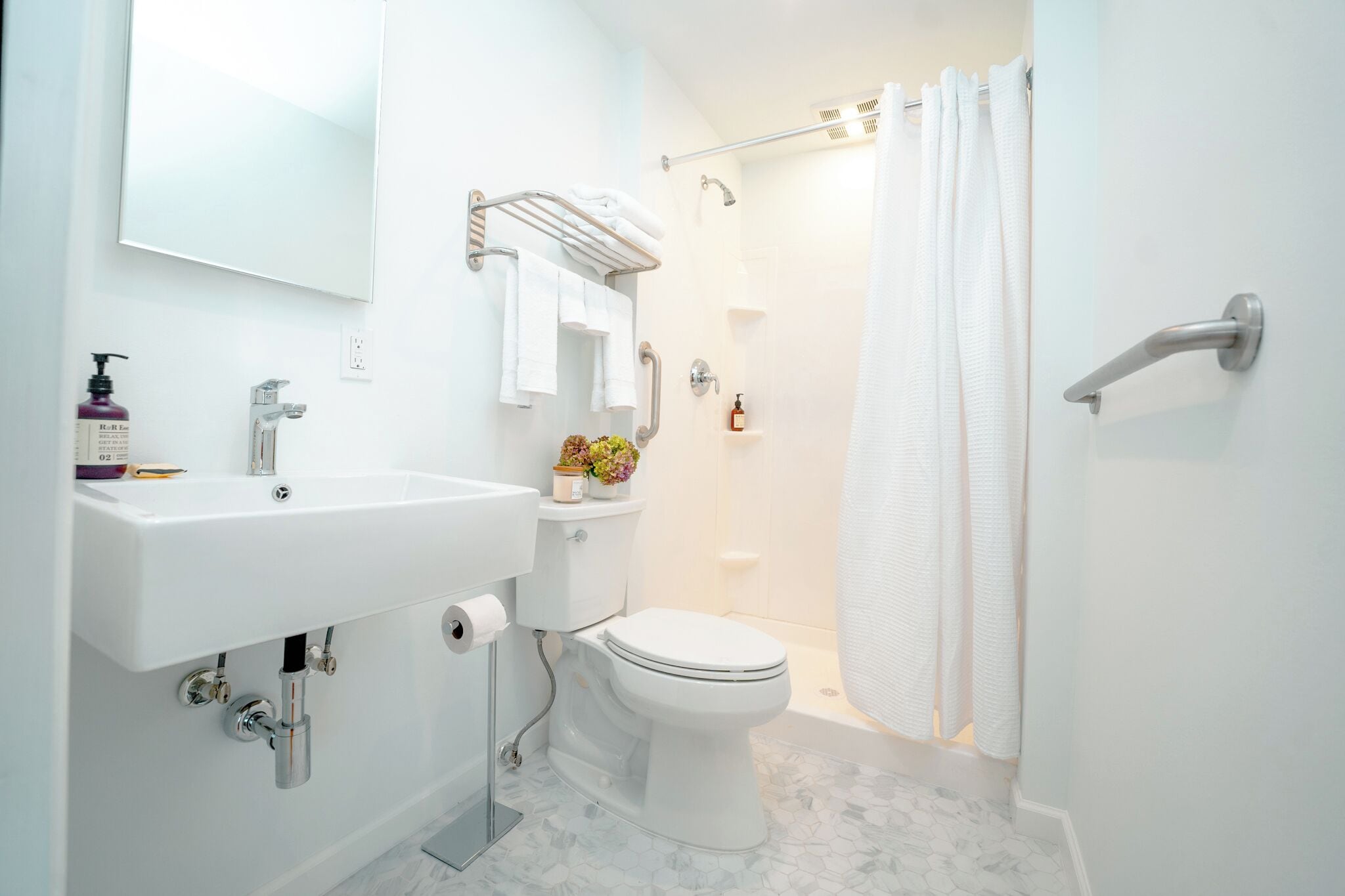 Une salle de bain moderne avec un lavabo, des toilettes et une douche, le tout de couleur blanche.