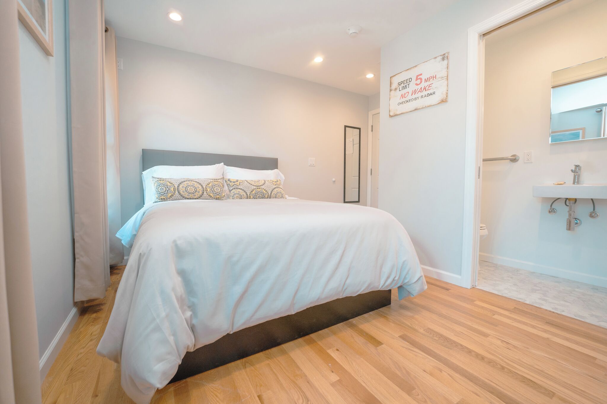 A bedroom with a bed, a bedside table, a mirror, and a door leading to a bathroom.