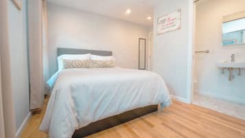 A bedroom with a bed, a bedside table, a mirror, and a door leading to a bathroom.