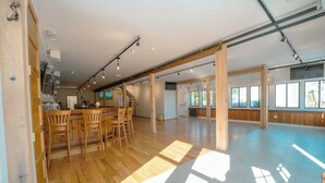 Une pièce spacieuse dotée d’un plancher en bois, d’un coin bar avec des tabourets et de grandes fenêtres laissant entrer la lumière naturelle.