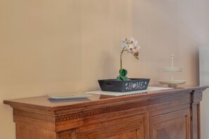 A wooden desk with a vase of white orchids, a small plant, and a decorative tray with the word "HOME" on it.