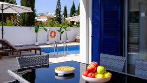 A poolside area with a table, chairs, a bowl of fruit, and a lounge chair. - Adamante Luxury Villa by Nomads (Paphos)