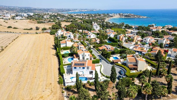 An aerial view of a coastal residential area with houses, a beach, and a clear blue sea. - Adamante Luxury Villa by Nomads (Paphos)