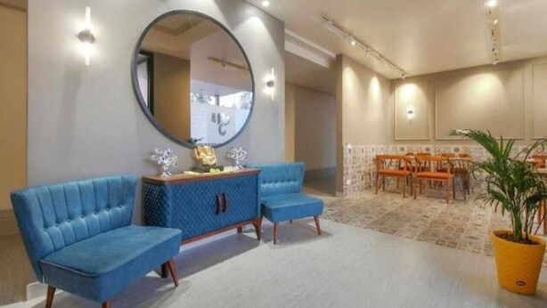 A room with a blue sofa, a round mirror, a wooden cabinet, and a dining area with orange chairs. - Hotel The Golf (Lucknow)