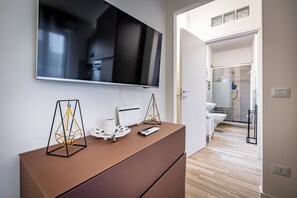 A modern room with a flat-screen TV mounted on the wall, a brown dresser, a white toilet, and a shower area visible through an open door. - YiDCefalonia (Florence)
