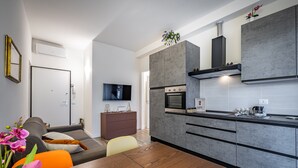 A modern kitchen with grey cabinets, a built-in oven, and a flat-screen TV mounted on the wall. - YiDCefalonia (Florence)