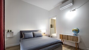 A modern bedroom with a bed, bedside table, lamp, and a globe on a wooden cabinet. - YiDCefalonia (Florence)