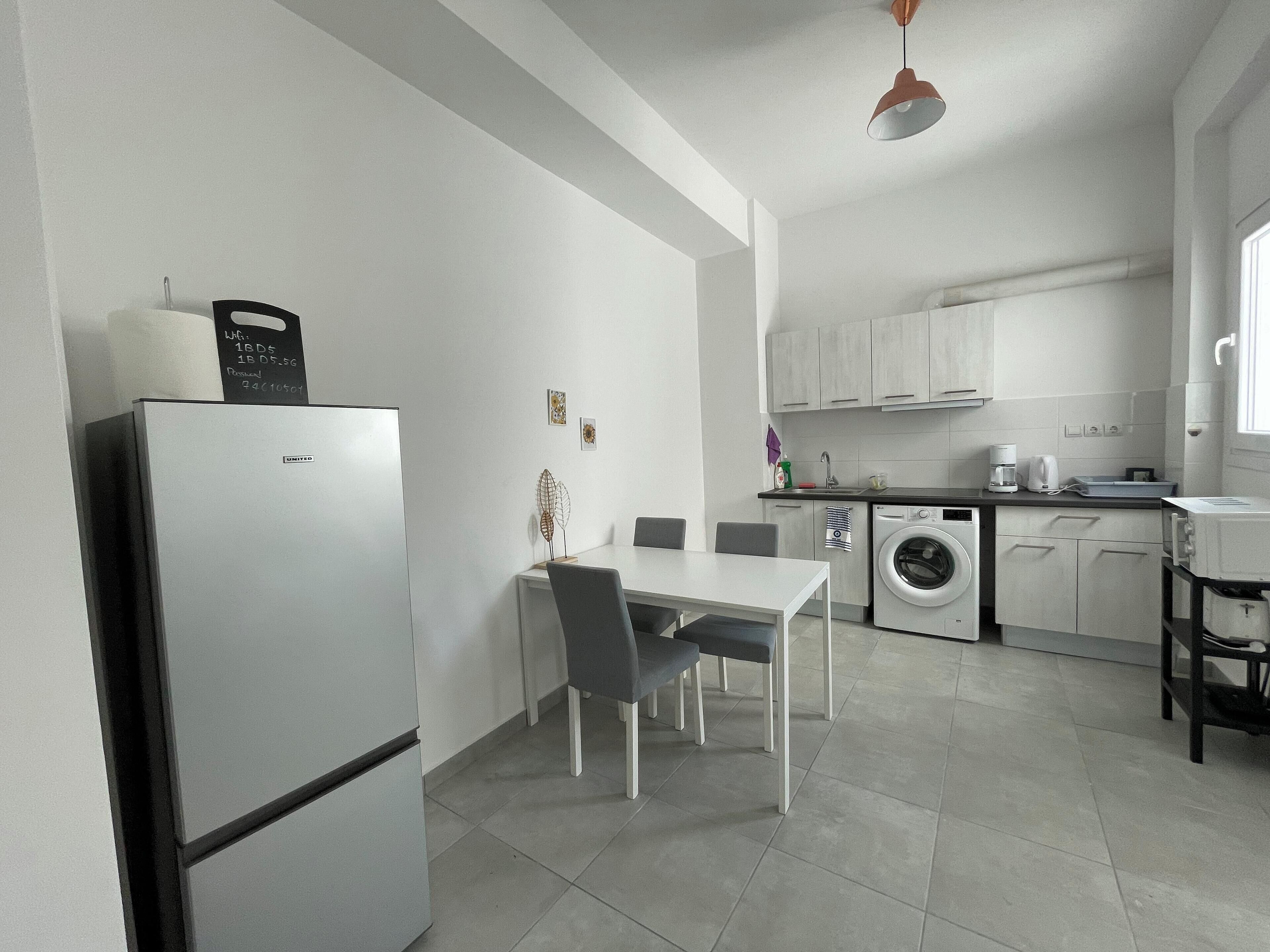 A compact kitchen with a refrigerator, a washing machine, and a dining area with a table and chairs.