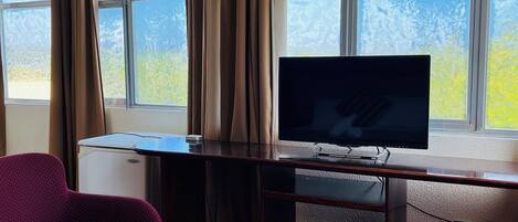 A room with a television, two chairs, a small table, and a window with curtains.