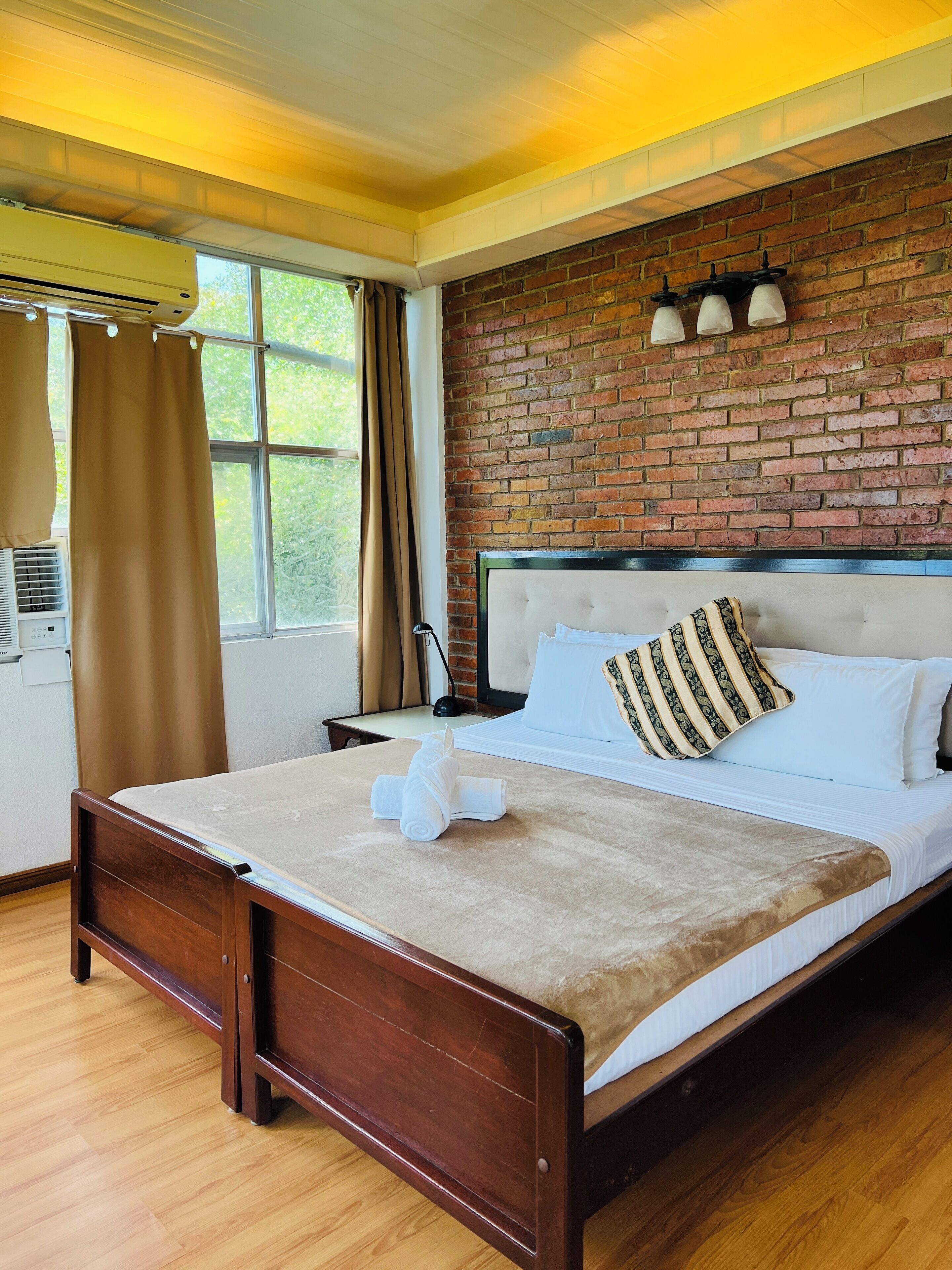 Une chambre d’hôtel avec un mur en briques, un lit en bois, une fenêtre avec des rideaux et une table de chevet avec une lampe.