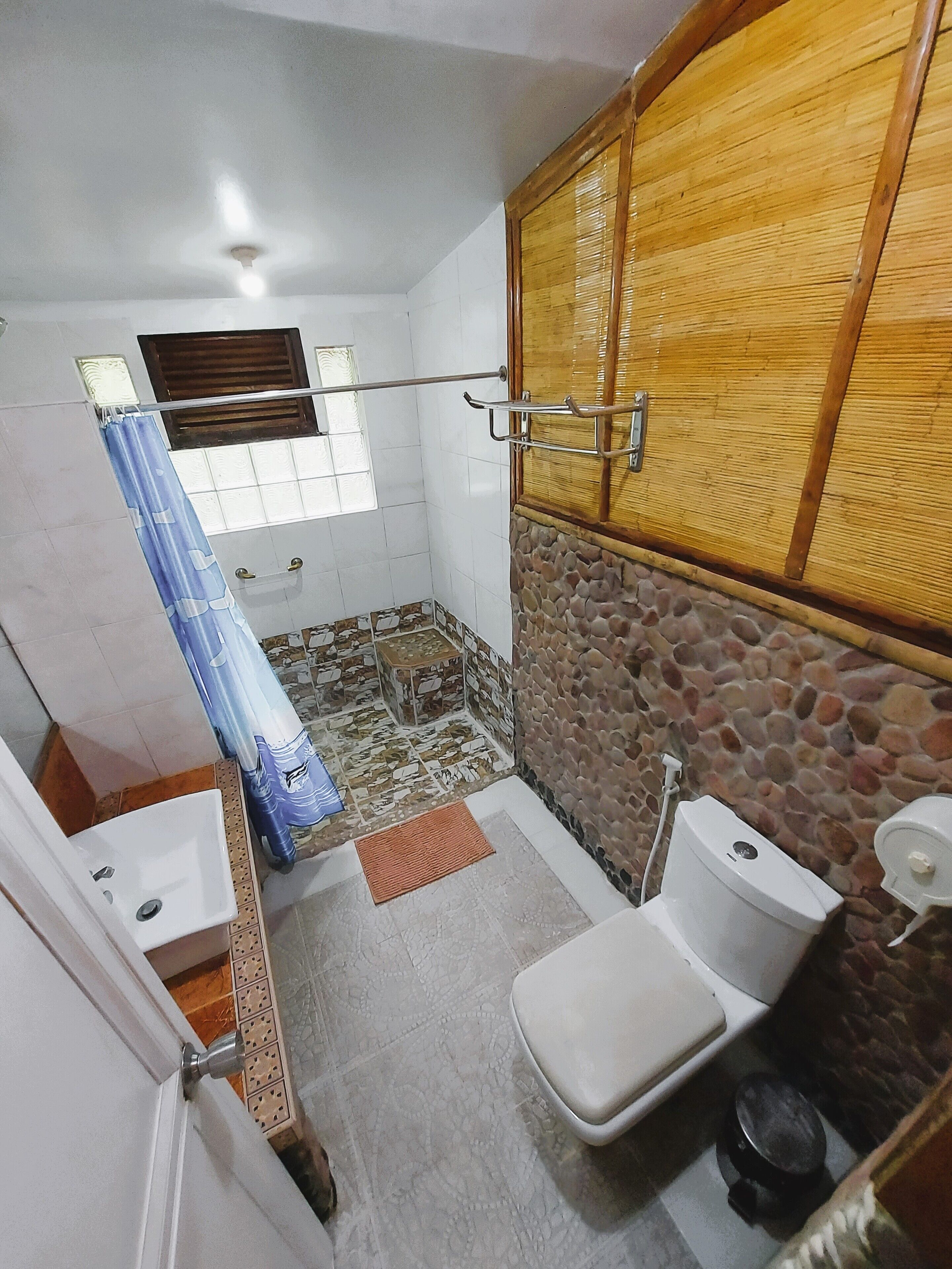 A small bathroom with a toilet, sink, shower, and a stone wall.
