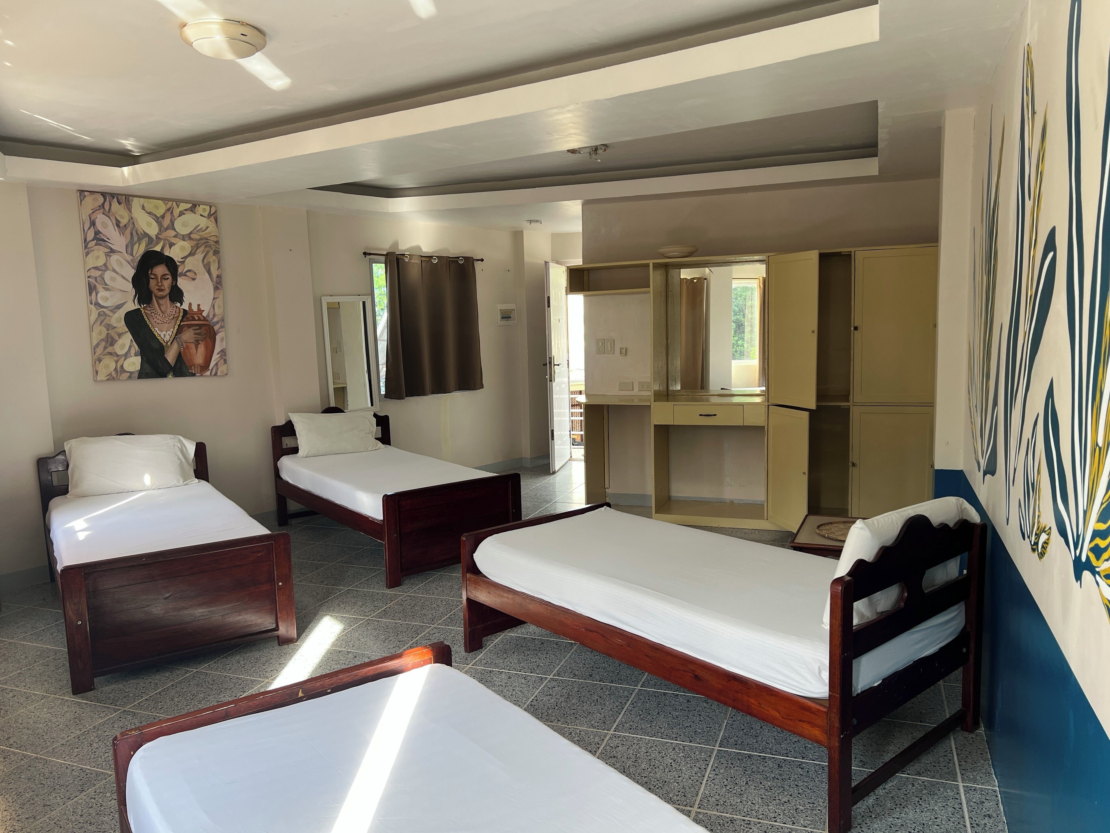 A hotel room with three wooden beds, a large mirror, a wardrobe, and a painting on the wall.