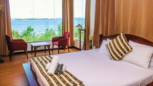 Une chambre d’hôtel avec un grand lit, deux fauteuils rouges, une petite table et une vue sur une étendue d’eau.