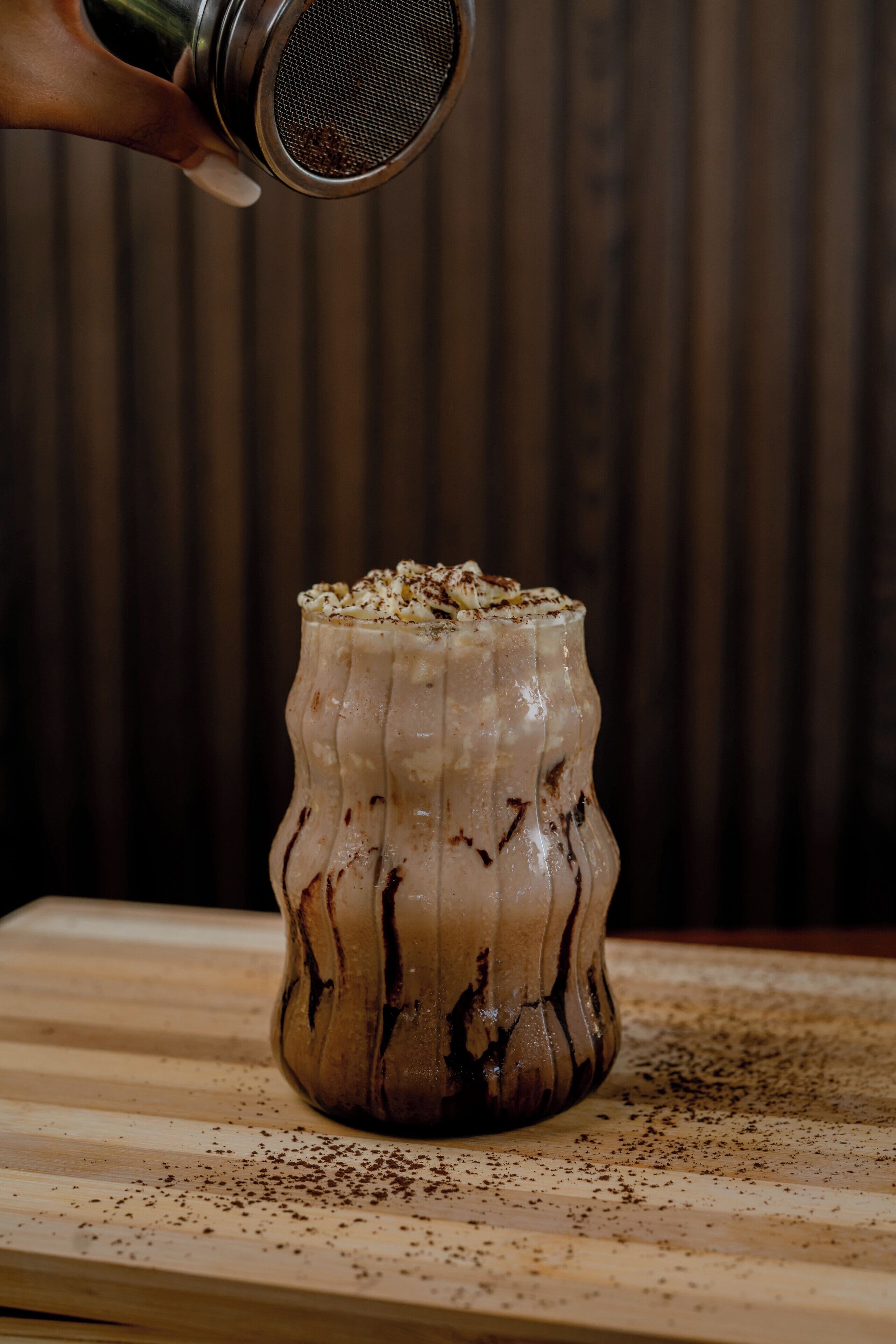 A hand sprinkling seasoning over a textured beverage in a glass.