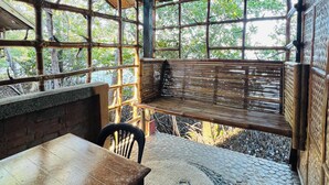 Un espace extérieur abrité, aménagé avec une table et des chaises, entouré d’une structure en bambou et doté d’un sol carrelé en pierre.