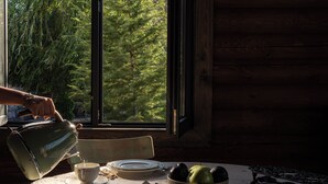 A rustic wooden cabin interior with a dining table set for tea, a bowl of fruit, and a skateboard.