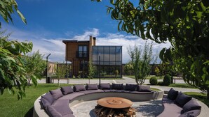 A modern outdoor seating area with a circular design, a fire pit in the center, and a building with large windows in the background.