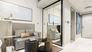 A modern hotel room with a sofa, two round tables, a lamp, and a large mirror.