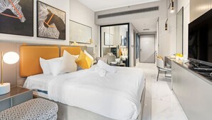 A modern hotel room with a large bed, a desk, and a kitchenette.