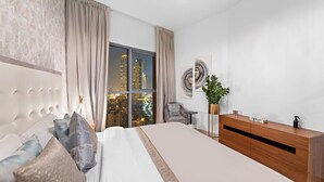 A modern hotel room with a large bed, a wooden dresser, a city view, and a chandelier.