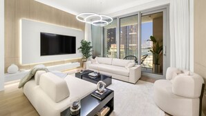 Una sala de estar moderna con un televisor de pantalla plana grande, un sofá blanco, una mesa de centro y vistas a un paisaje urbano a través de amplios ventanales.