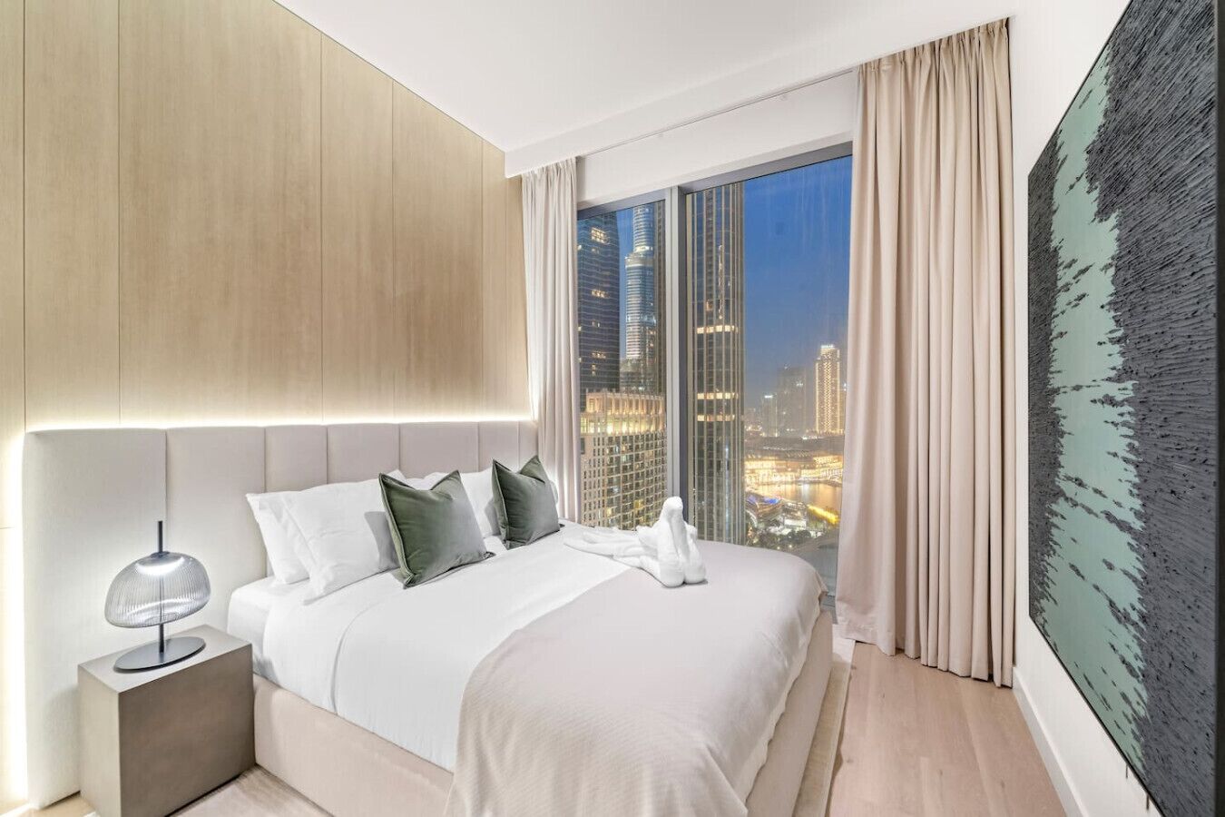 Ein modernes Hotelzimmer mit einem großen Bett, einem Nachttisch, Blick auf die Stadt und einem großen abstrakten Gemälde.