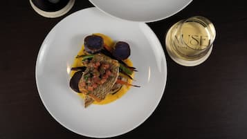 A dining table with a white plate of food, a glass of white wine, and a black cup.