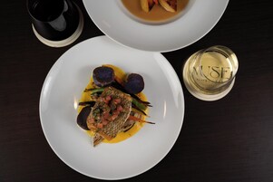 A dining table with a white plate of food, a glass of white wine, and a black cup.