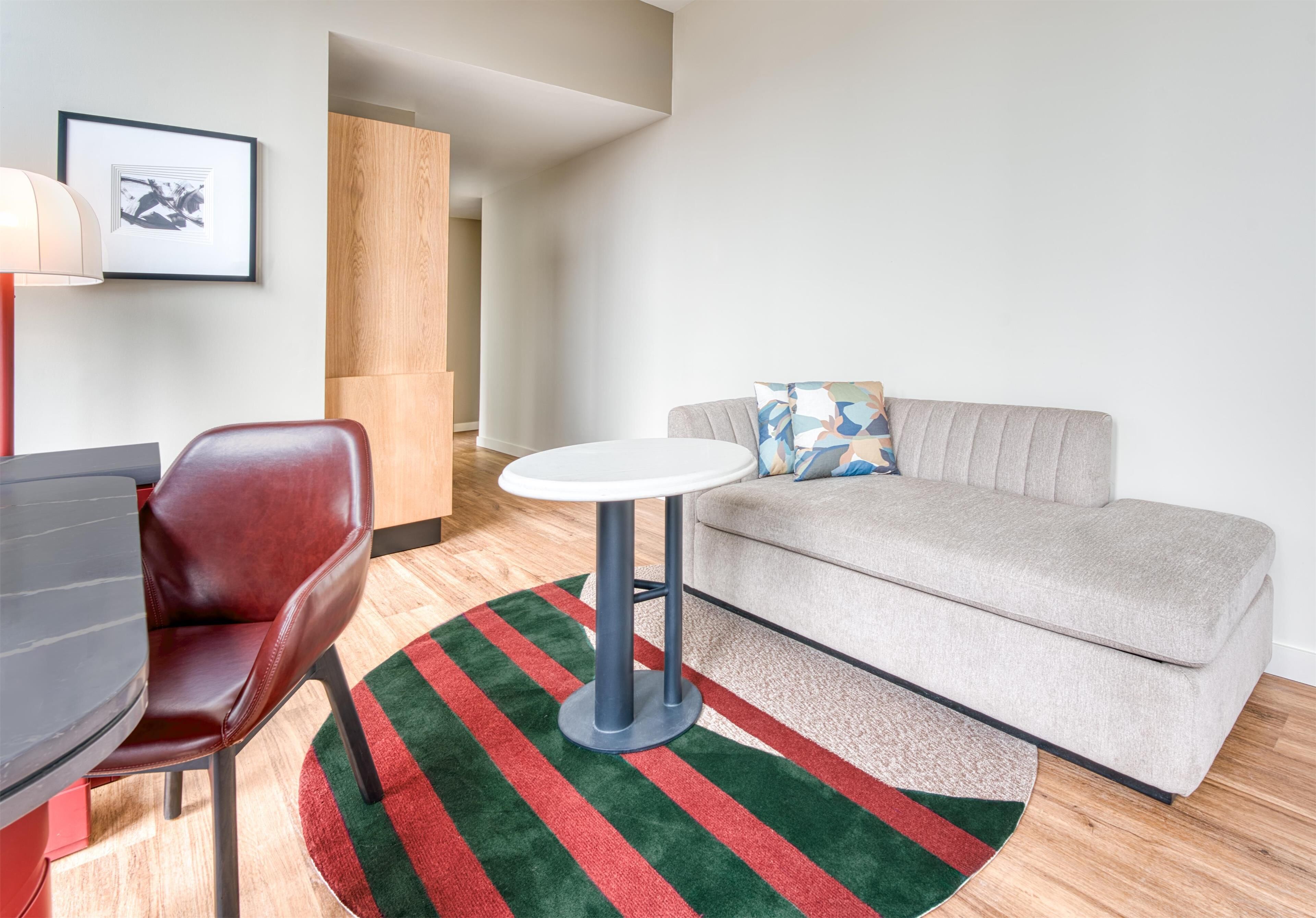A modern living room with a grey sofa, a red chair, a round table, and a striped rug.