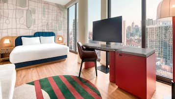A hotel room with a bed, desk, chair, TV, and large windows with a city view.