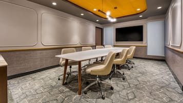 Un salón de conferencias con una larga mesa, varias sillas, una pantalla grande e iluminación empotrada en el techo.