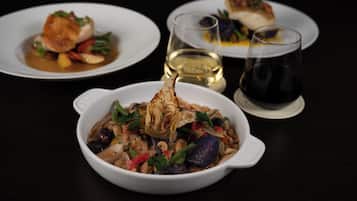Une table à manger avec trois assiettes blanches remplies de nourriture, deux verres de vin et un saladier blanc contenant une variété de légumes et de fruits de mer.
