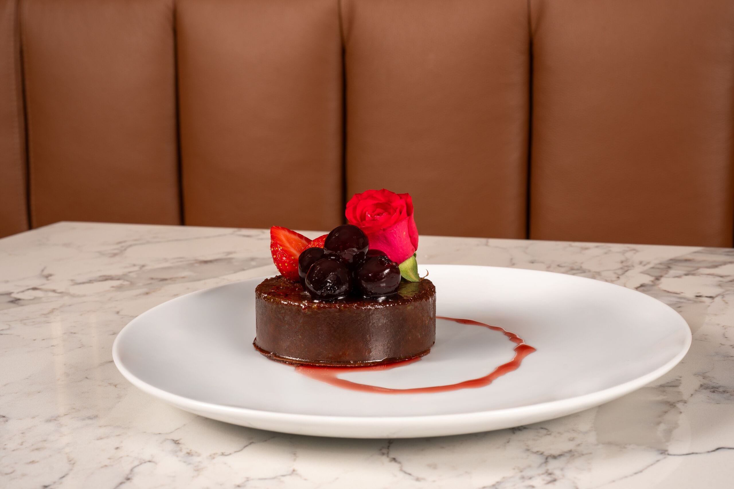 Un postre sobre un plato blanco, con una mesa de mármol y una silla tapizada de color marrón al fondo.