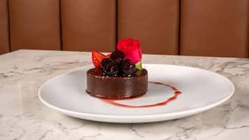 Un postre sobre un plato blanco, con una mesa de mármol y una silla tapizada de color marrón al fondo.