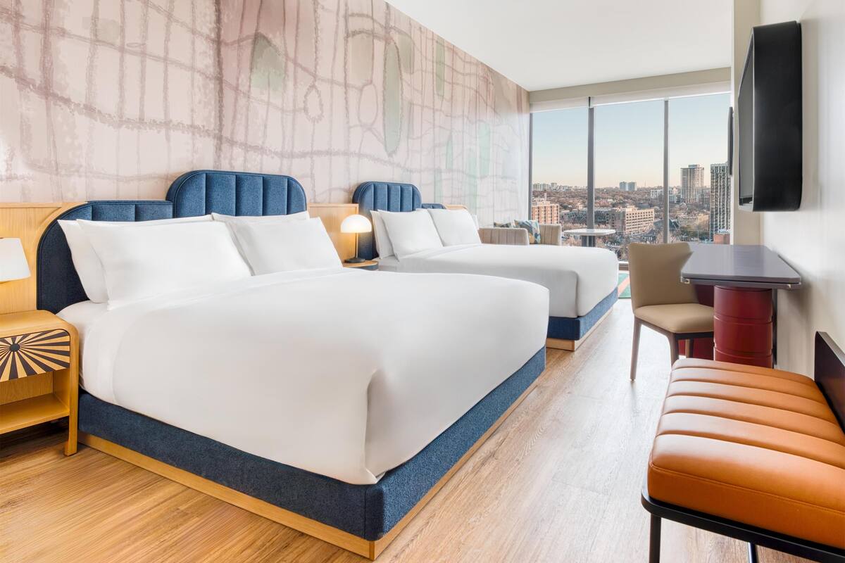 Ein Hotelzimmer mit zwei Betten, einem Fernseher und Blick auf die Stadt.