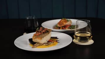 Een eettafel met twee borden eten en een glas witte wijn.
