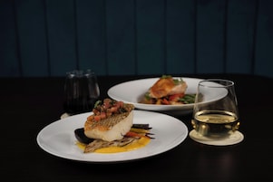 Een eettafel met twee borden eten en een glas witte wijn.