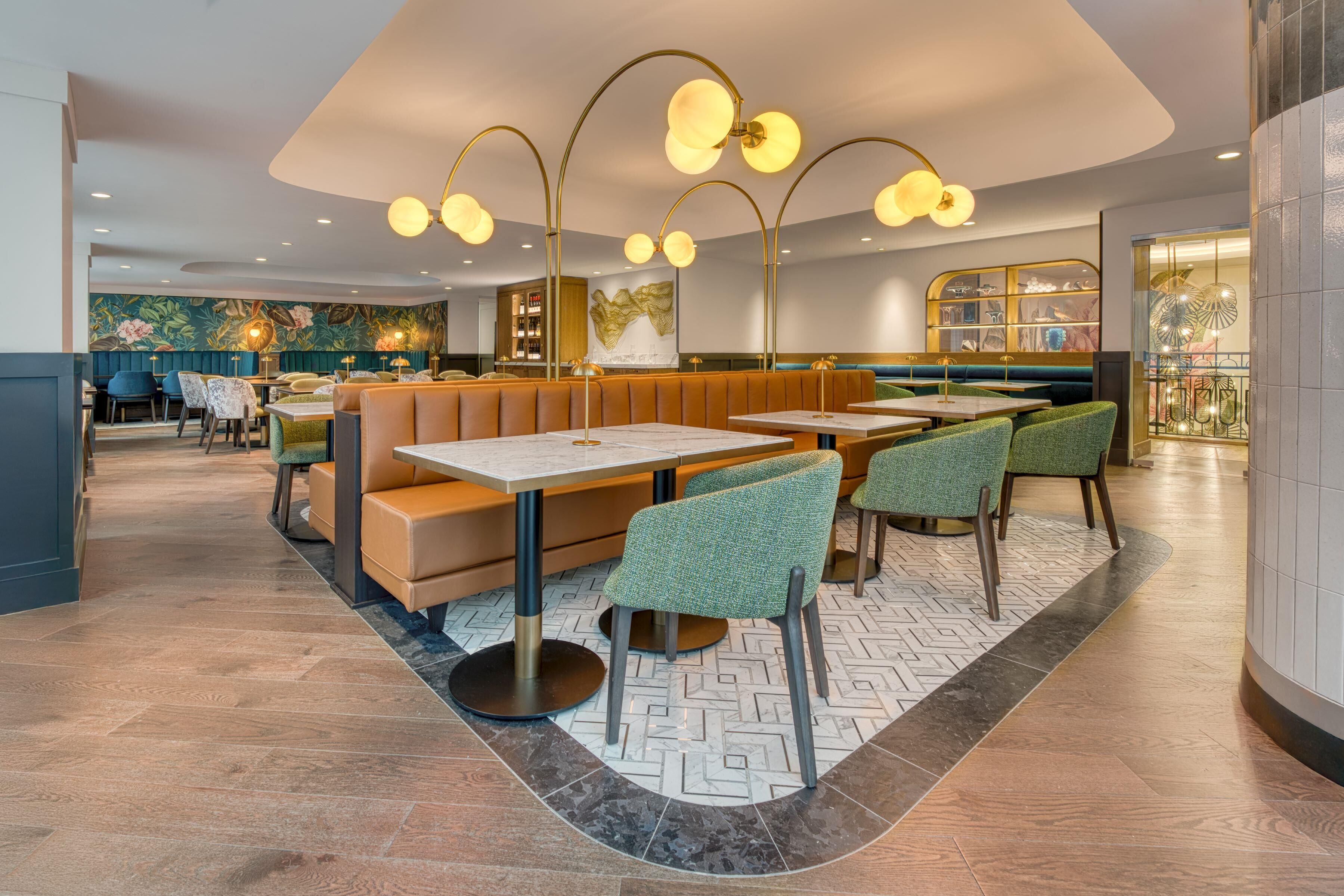 Een modern restaurantinterieur met zitjes, tafels en groene stoelen.