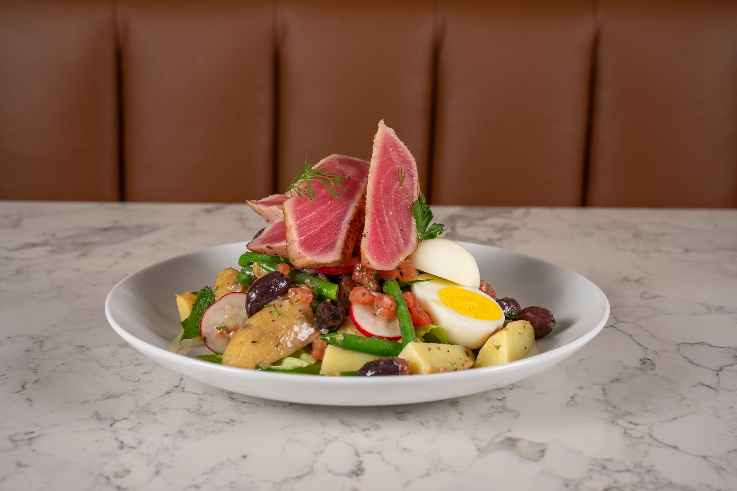A white plate with a salad on a marble table.