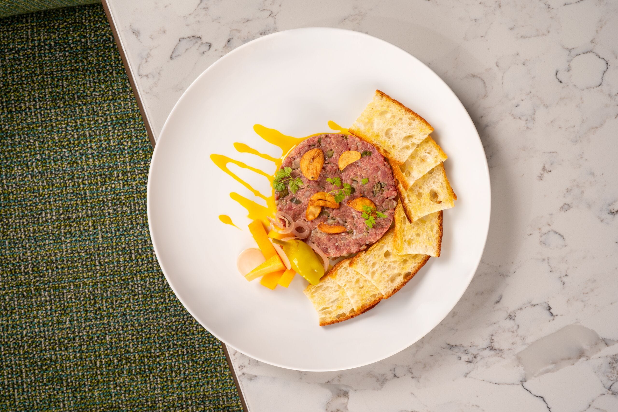 A plate of food with a slice of meat, vegetables, and bread on a white plate.